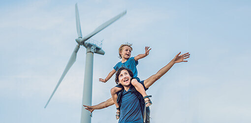 A smiling father and son in front of a wind turbine against a blue sky