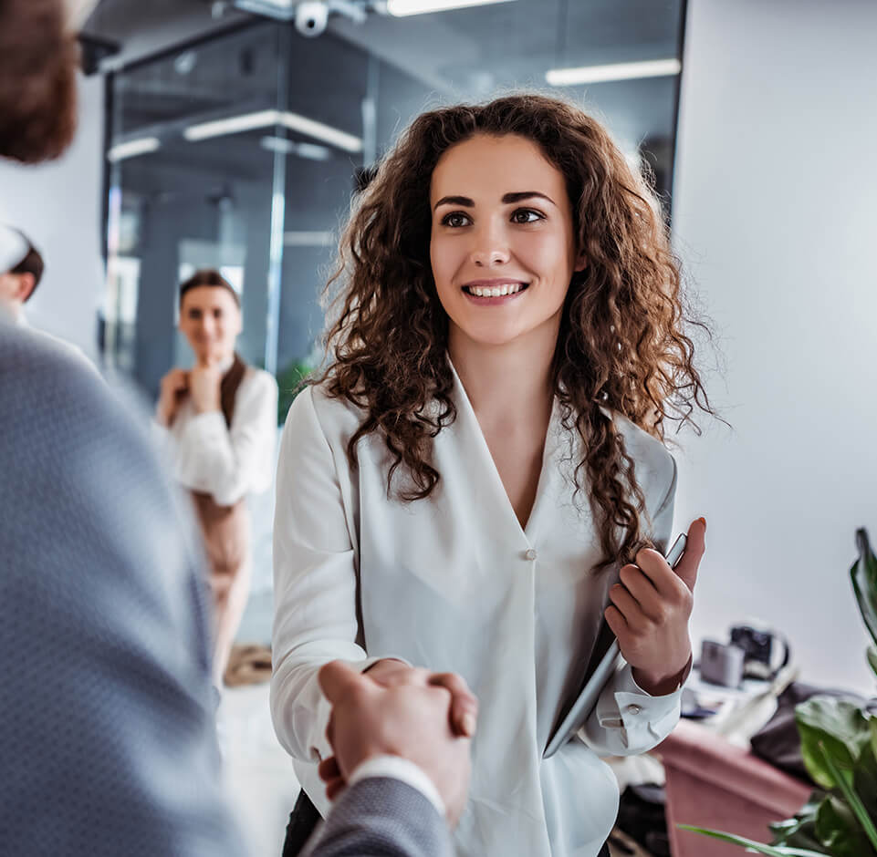 A smiling customer service representative shakes hands with a client in an office. Engaging with customers is easy when the customer information system is well-optimized.